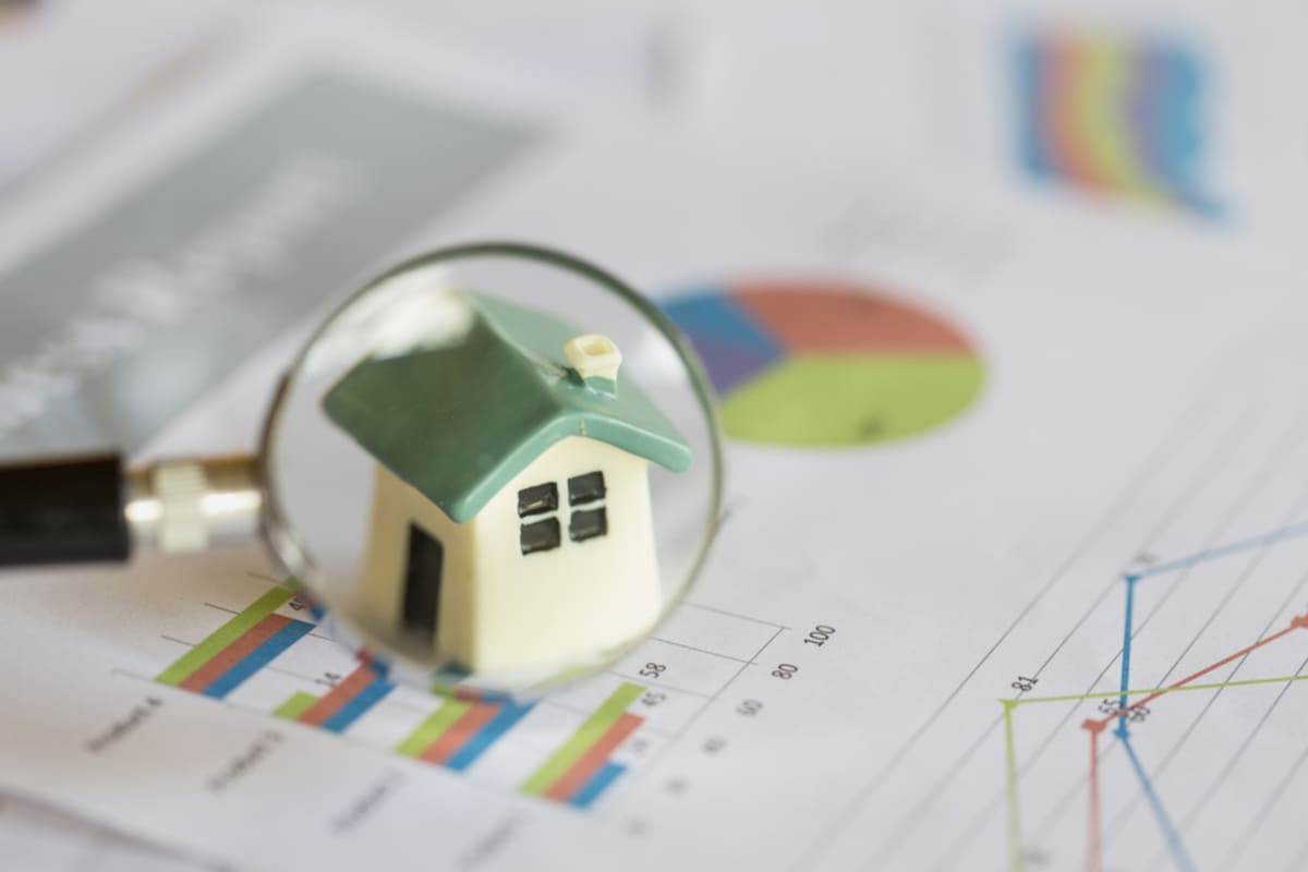 A magnifying glass over house next to charts, conducting research to determine rental rates concept