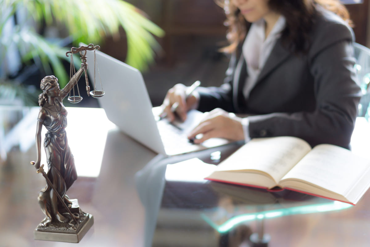 A woman working on her laptop next to a book and figure holding a scale, legal tenant eviction concept.