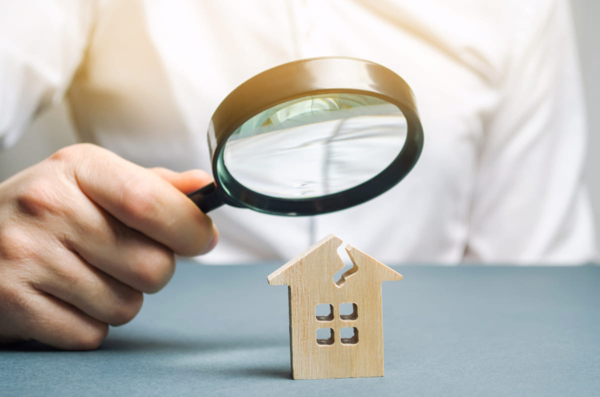 Someone holding a magnifying glass above a small damaged home, rental property management concept