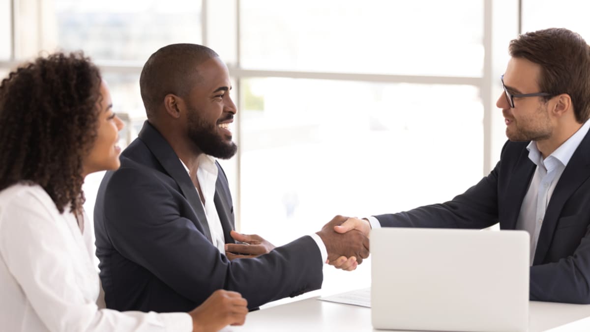 Three businesspeople at a table, two shaking hands, property management companies Indianapolis concept