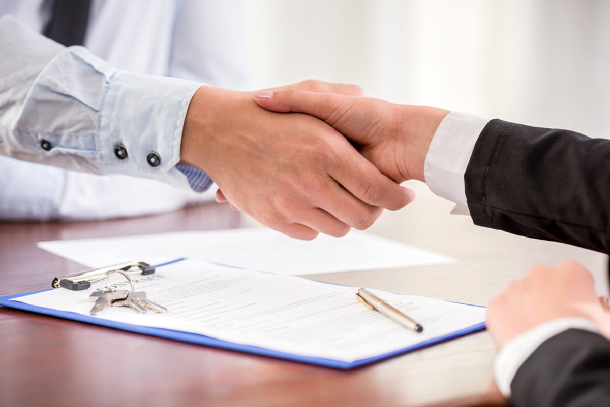 Two people shaking hands over a contract